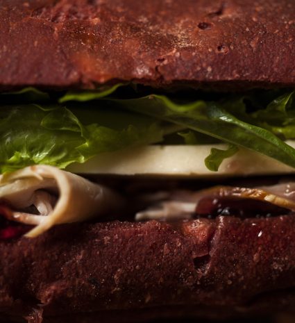 Sandwich au pain brun garni de feuilles vertes et d’une tranche pâle