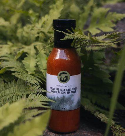 Bouteille de sauce BBQ aux bolets fumés parmi des fougères