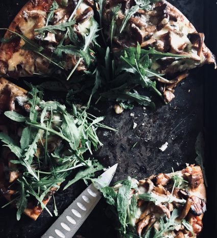 Morceaux de pizza aux champignons sauvages et à la roquette sur une surface noire