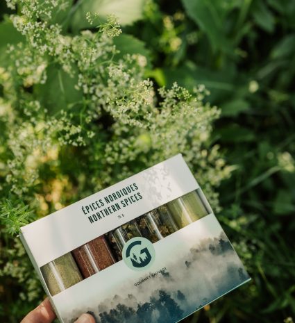 Coffret Épices nordiques tenu devant des plantes en fleurs