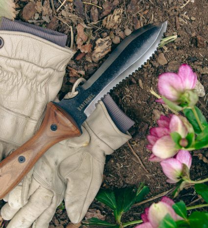 Couteau hori hori et gants de travail sur un sol forestier