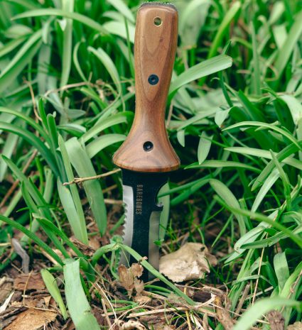 Couteau hori hori planté dans l’herbe et les feuilles mortes