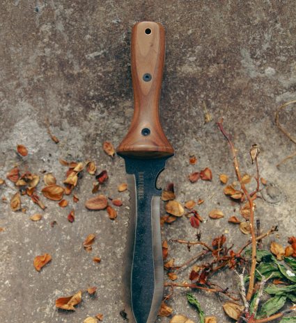 Couteau hori hori à manche de bois sur un sol couvert de feuilles