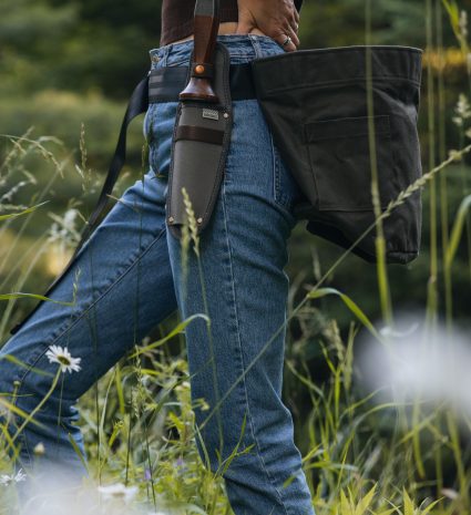 Sac de récolte noir porté à la taille dans une prairie