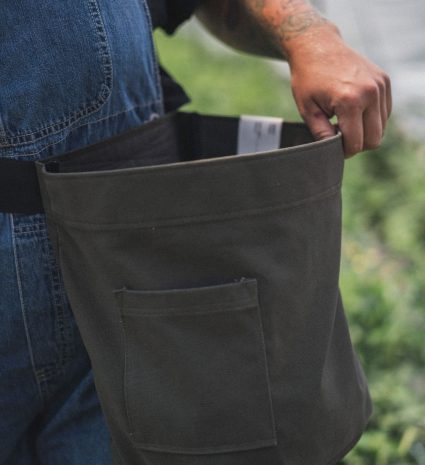 Sac Récolte en toile foncée tenu ouvert devant un feuillage