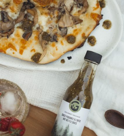 Bouteille de sauce piquante à l’ortie et au sapin près d’une pizza aux champignons