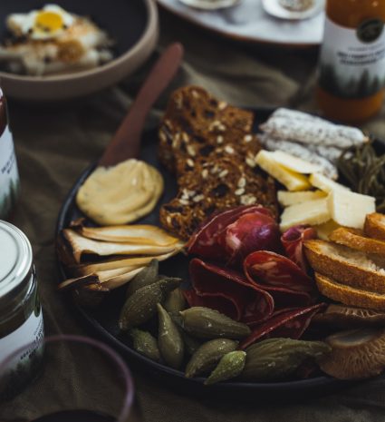 Gousses d’asclépiades marinées sur une assiette de fromages et de pain
