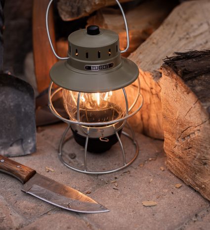 Lanterne rechargeable allumée près de bûches et d’un couteau