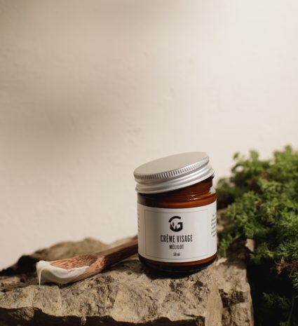 Pot de crème visage au mélilot posé sur une pierre avec une spatule