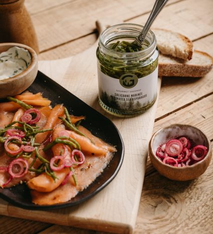 Pot de salicorne marinée ouvert avec cuillère sur une planche de bois