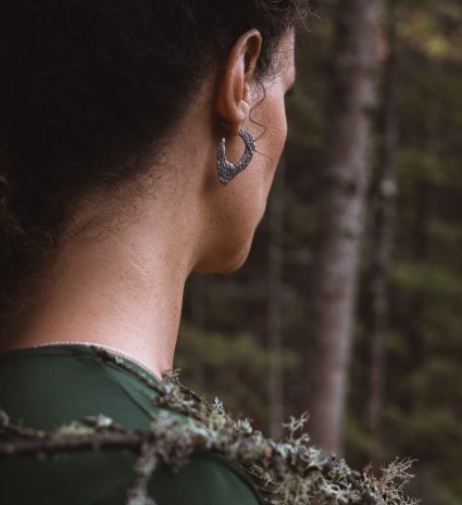 Les boucles d’oreilles Lichen pendent au lobe devant un sous-bois flou