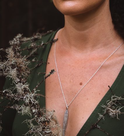 Un collier en argent avec un pendentif en forme de feuille, entouré de mousse et de lichen.