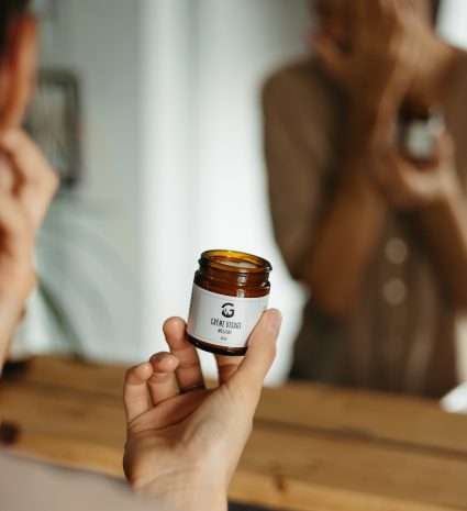 Pot de crème visage au mélilot tenu devant un miroir
