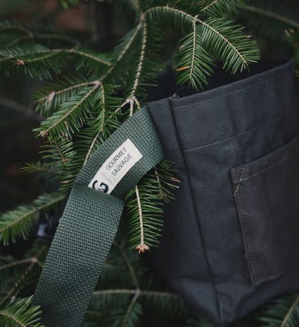 Sac de récolte pour apprenti parmi des branches de conifère