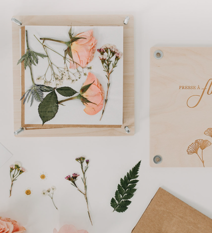 Presse à fleurs en bois avec fleurs et feuilles sur une table blanche