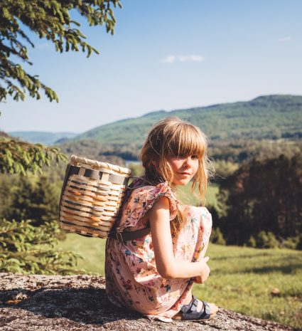 Jeune fille assise sur une roche avec un sac à dos en osier