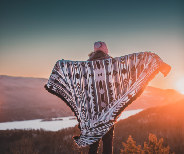 Personne avec une couverture sur un sommet enneigé au lever du soleil