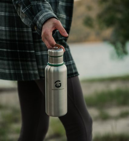 Gourde isotherme en acier inoxydable tenue près d’un plan d’eau