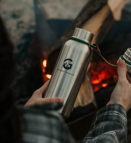 Gourde isotherme métallique tenue devant un feu de camp
