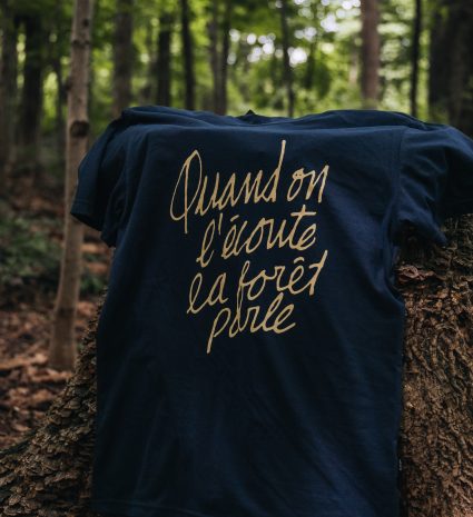 T-shirt « Quand on l’écoute, la forêt parle » posé sur une souche en forêt