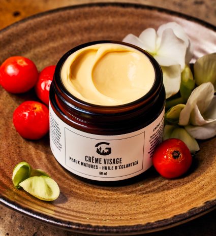 Crème visage à l’huile d’églantier dans un pot sur une assiette en bois