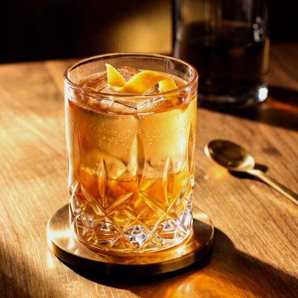 Cocktail ambré avec zeste d’agrume dans un verre taillé sur une table en bois